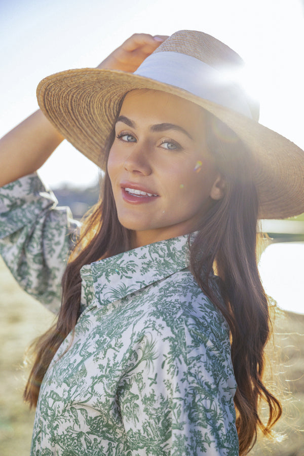 close up of a woman in a UPF 50+ green floral maxi dress with sun protection and a sun hat standing on a blurred grassy lawn at a country club 